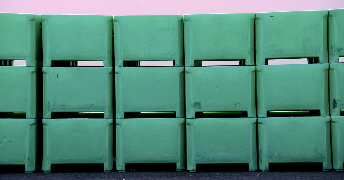 Row of green plastic tubs stacked against a pink wall. Industrial and storage concepts.