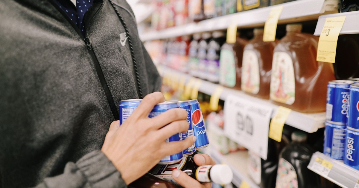 Close-up of an adult shopping for Pepsi and sauces in a grocery store aisle.