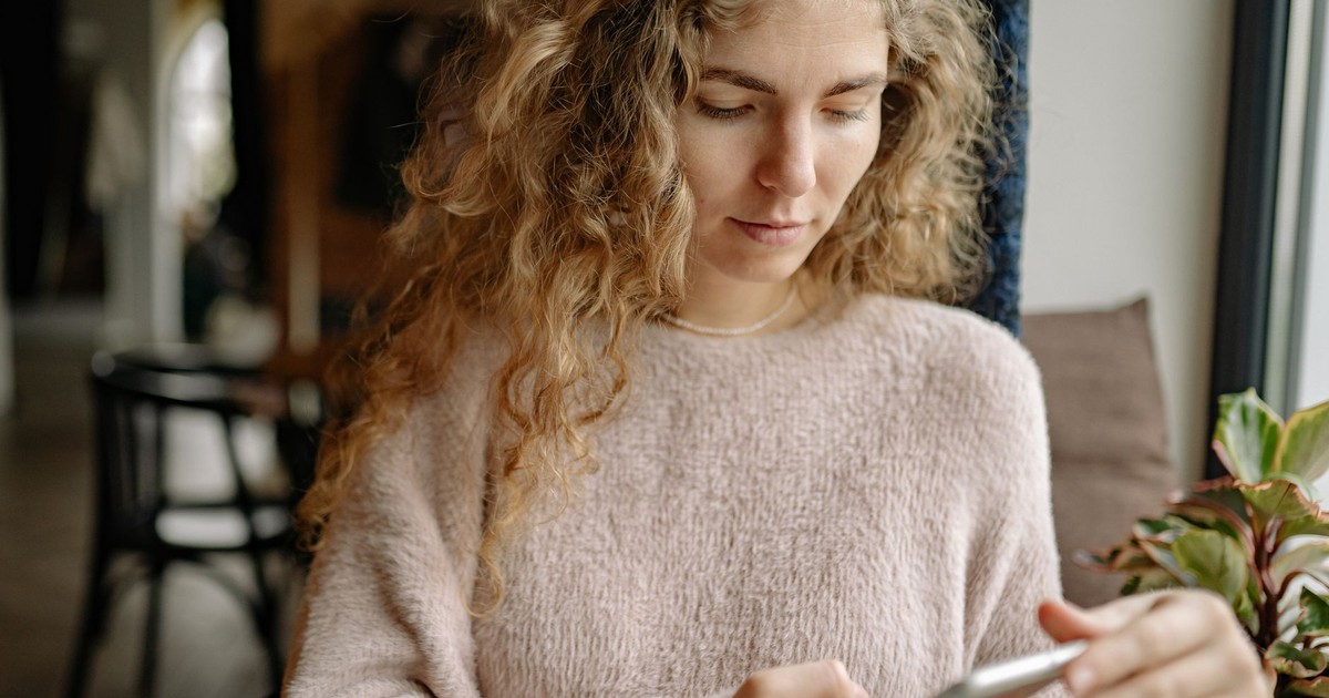 A woman in a cozy sweater using a smartphone in a relaxed indoor environment.