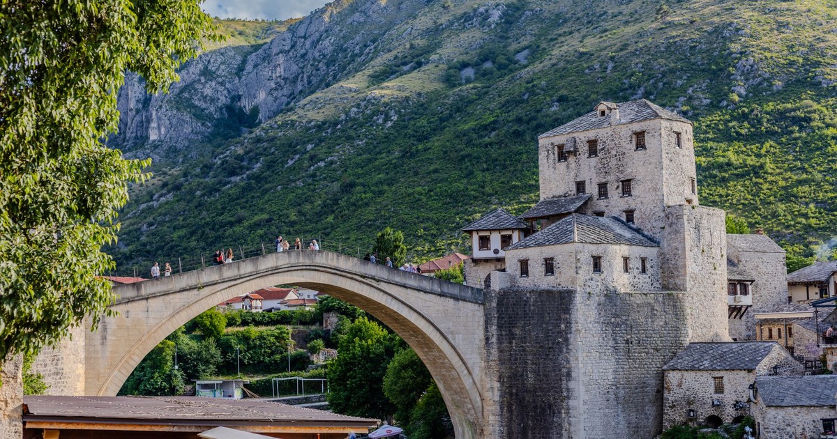 Scenic view of the historic arch bridge in Mostar with lush hills and the Neretva River.
