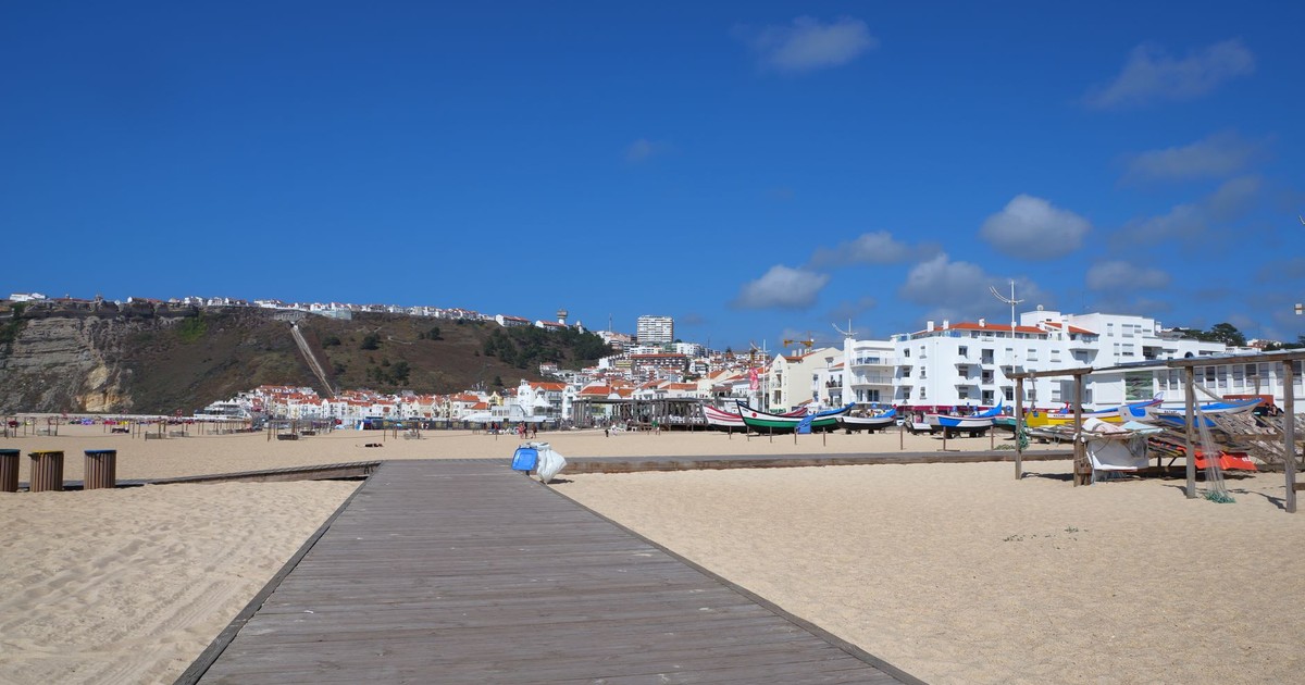Explore the beautiful beachside view of Nazaré, Portugal, featuring traditional boats and a bright blue sky.