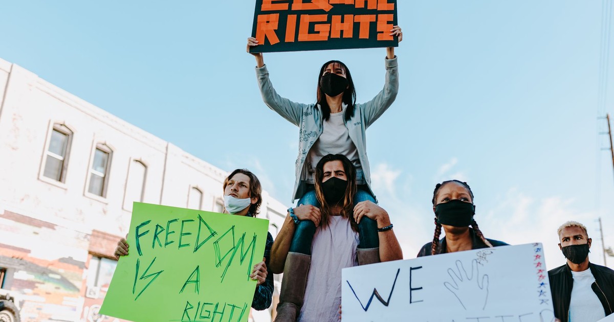 Diverse group of masked protesters holding signs for equality and rights outdoors.