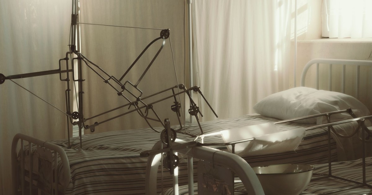 An empty hospital bed surrounded by medical equipment in a quiet, sunlit room.