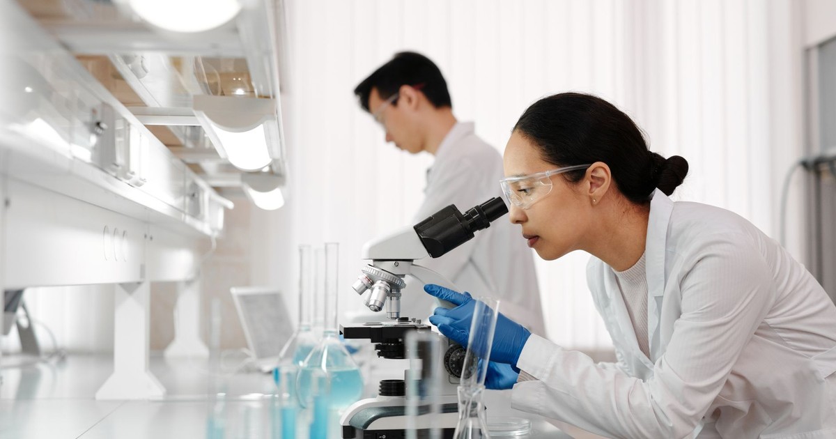 Two scientists in a lab examining samples with a microscope. Focus on scientific research and discovery.