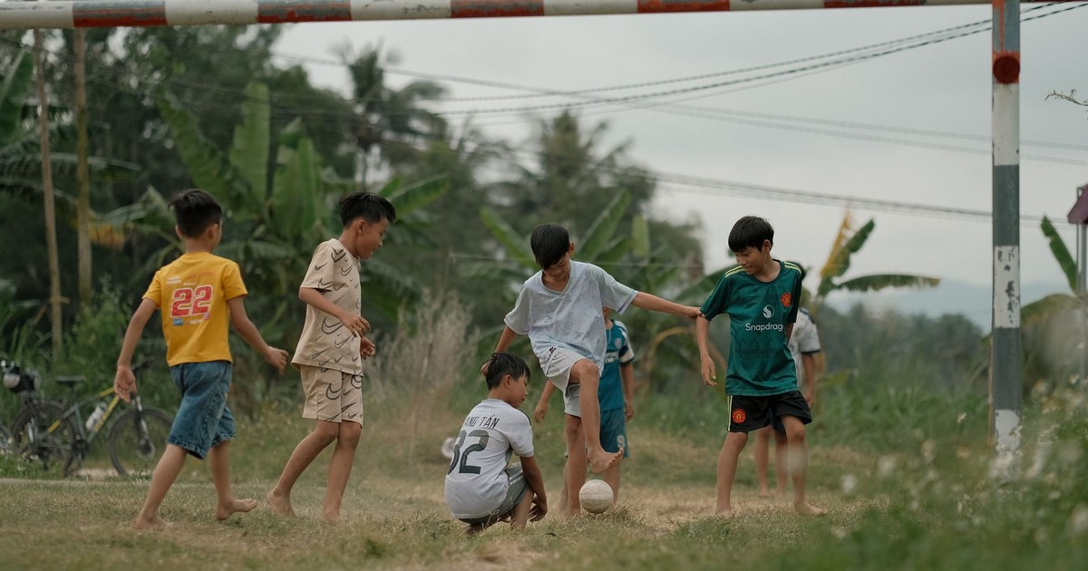 Group of boys playing soccer in a lush green field on a cloudy day.