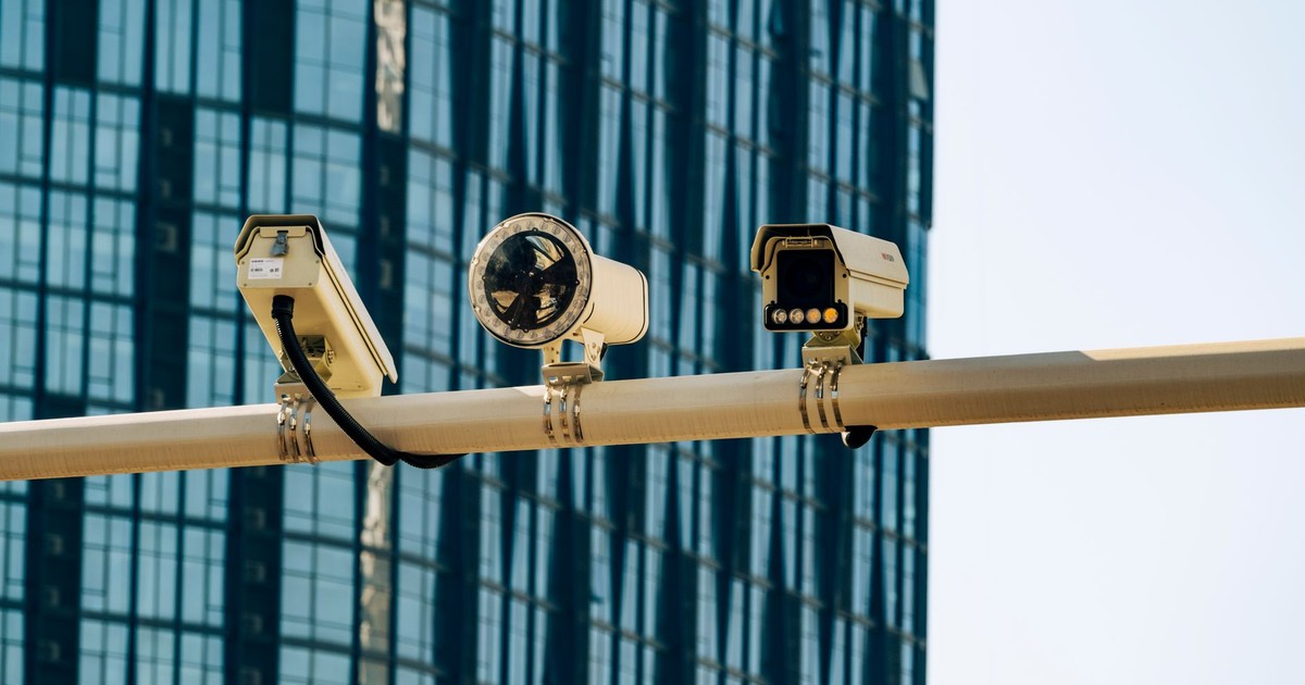 Surveillance cameras mounted on a pole in front of a modern glass building.