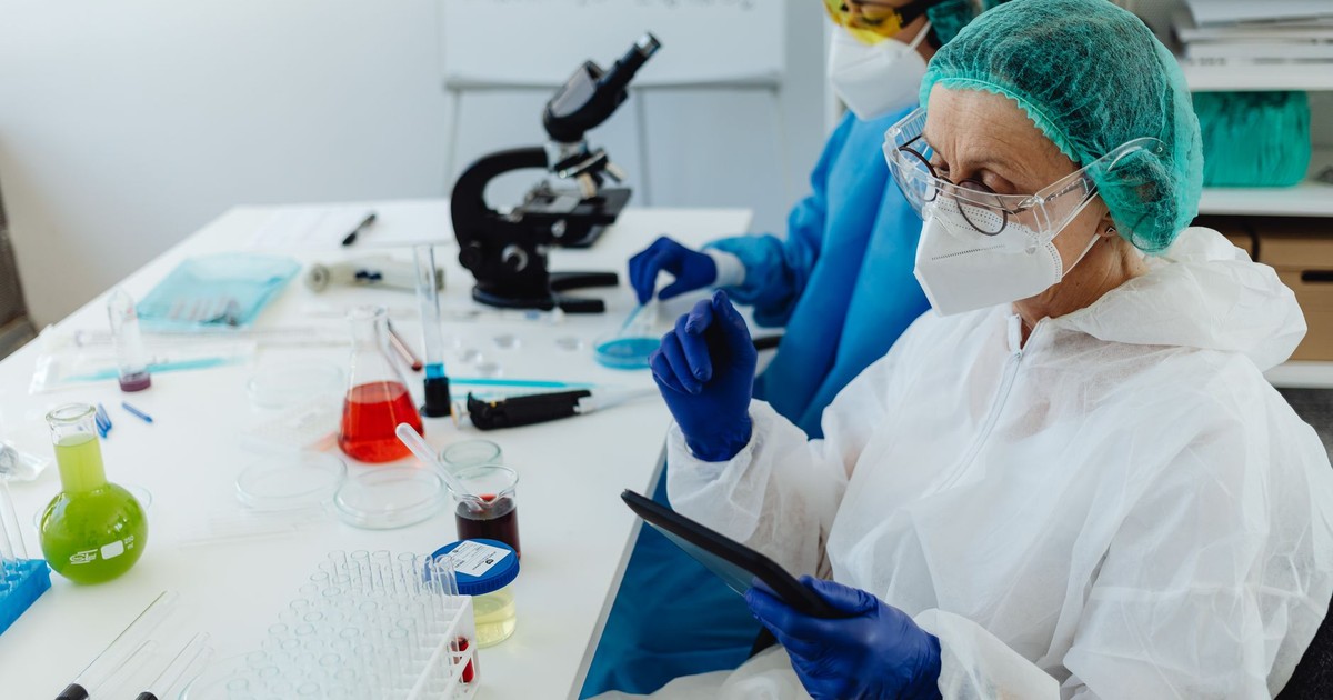 Researchers in PPE work in a lab with glassware and microscopes.