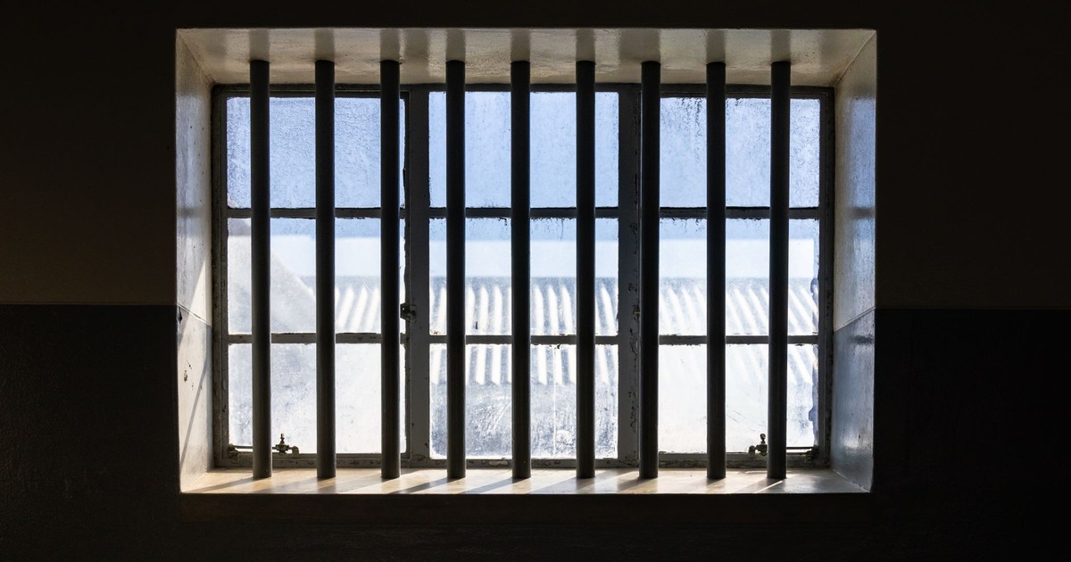 Sunlight streams through barred window of a prison cell, casting shadows and light patterns.