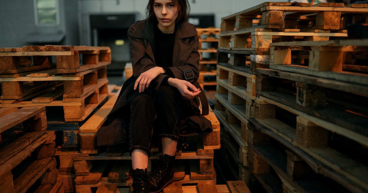 A woman posing on wooden pallets in an industrial warehouse setting.