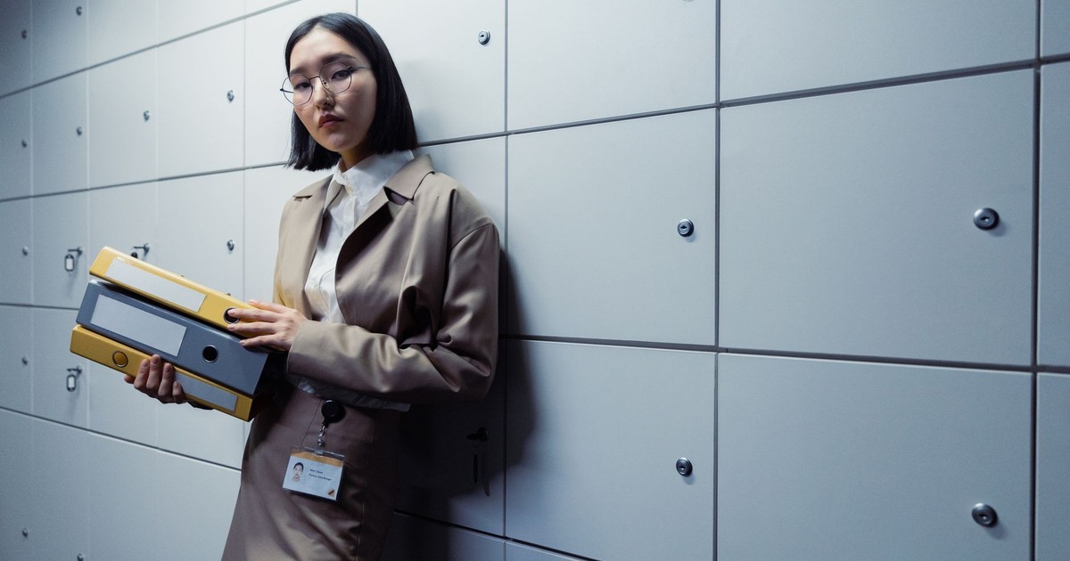 Businesswoman in office attire standing with documents, appearing poised in a modern office setting.