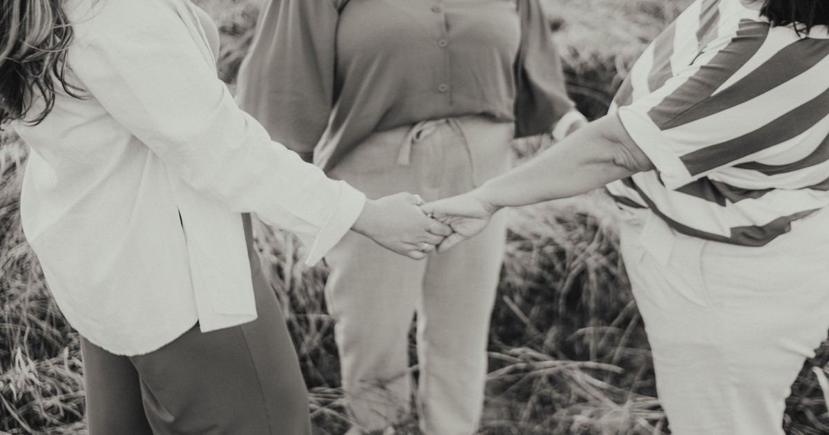 Three women standing in a meadow holding hands symbolizing friendship and unity.