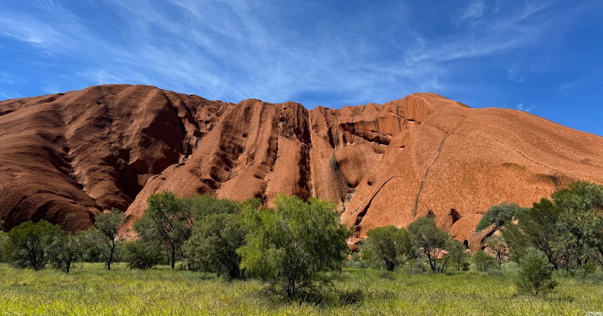 Stunning view of Uluru's red rock under a clear blue sky with lush greenery.