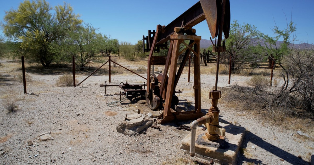Rusted pumpjack in arid desert setting with sparse vegetation and clear sky.