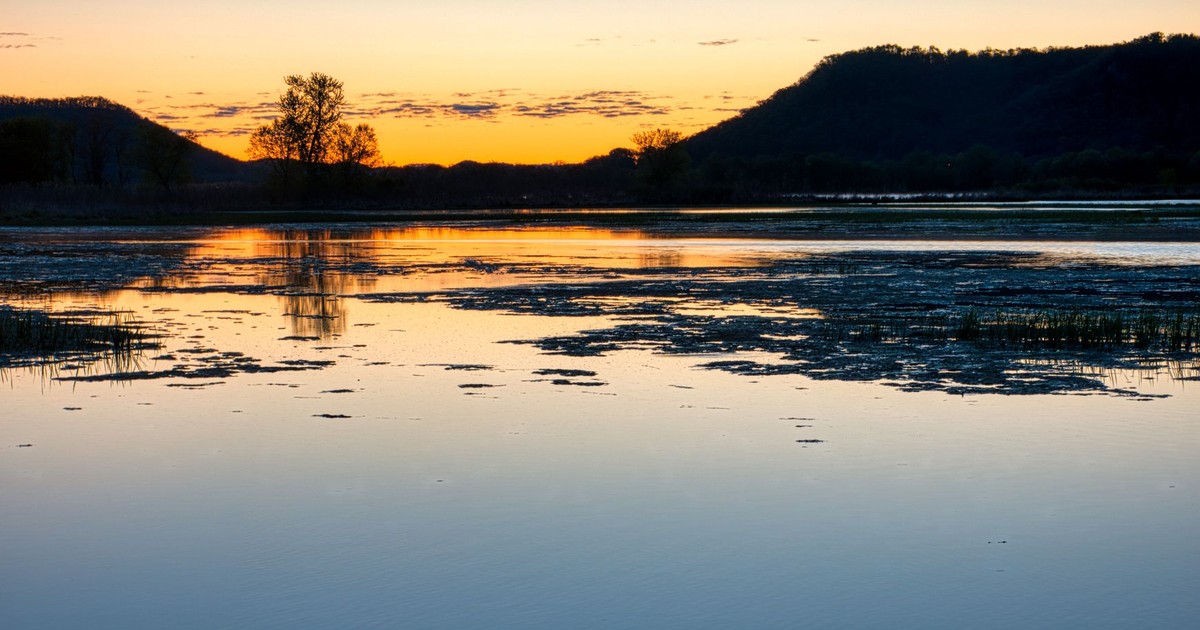 Peaceful sunset scene over Mississippi River with silhouette of distant hills and water reflection.