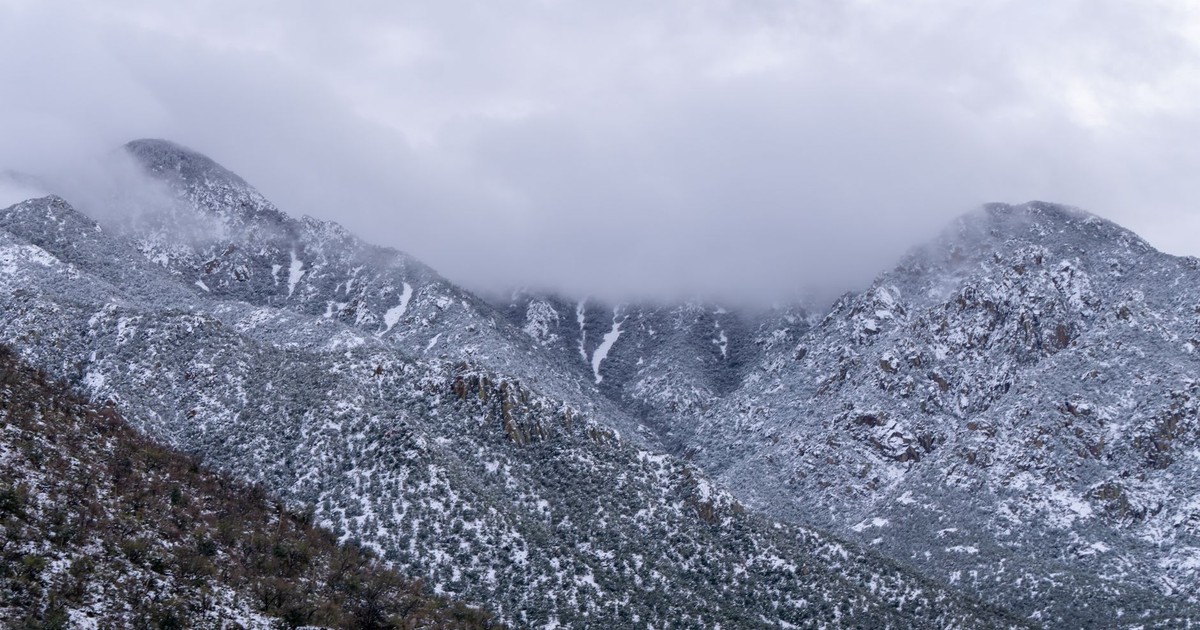 Snow-covered Arizona desert mountains with fog over the peaks, captured in a winter storm setting.