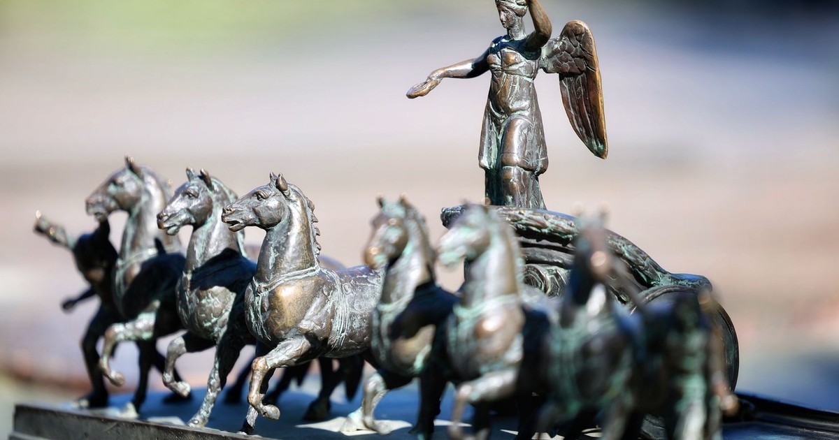 Detailed bronze sculpture of angel on chariot with horses, outdoor setting.