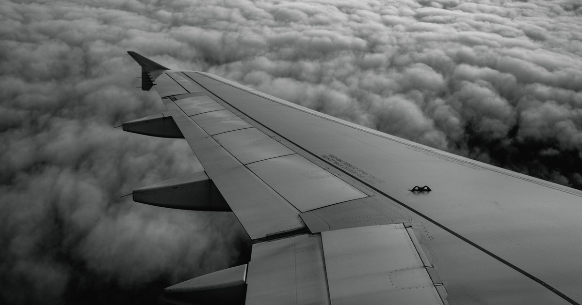 Aerial view from an airplane window showcasing a wing above a vast cloudscape.