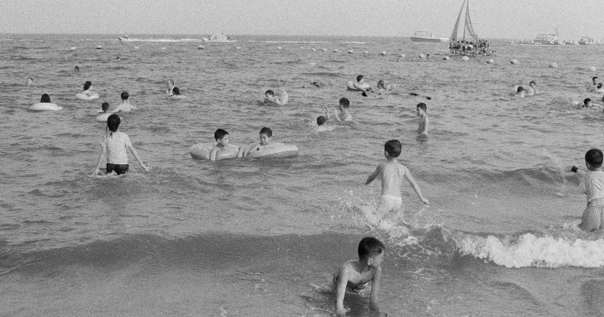 Black and white photo of children enjoying a day at the beach, playing in the ocean waves.