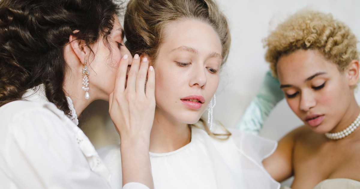 Three women in vintage fashion whispering secrets, showcasing elegant style.