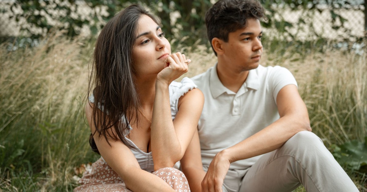 A thoughtful couple sitting together in a tranquil grassy field, enjoying the outdoors.