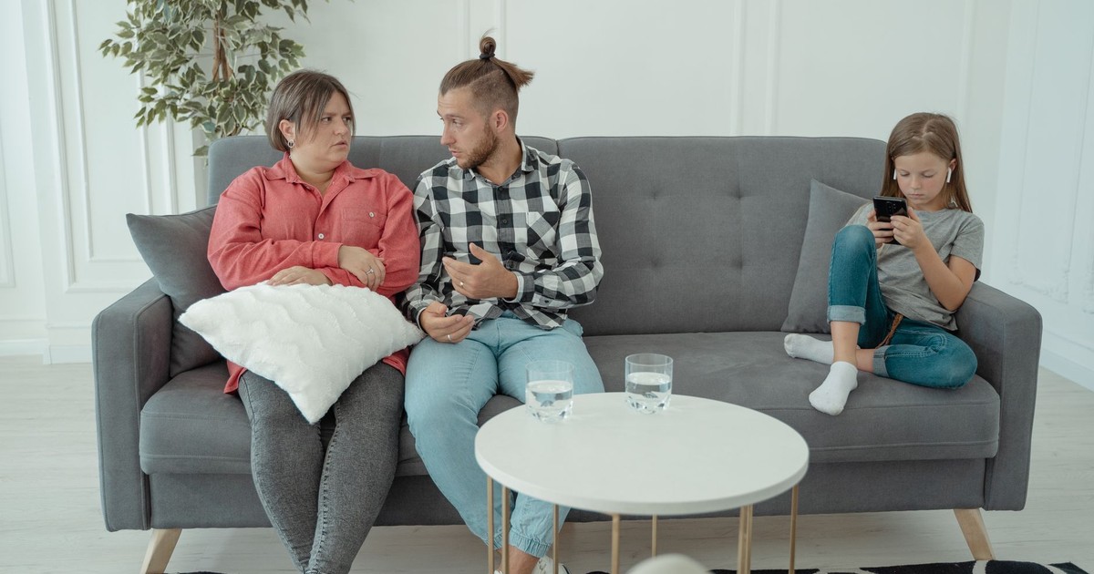 A family therapy session with parents discussing things while a child is absorbed in her smartphone.