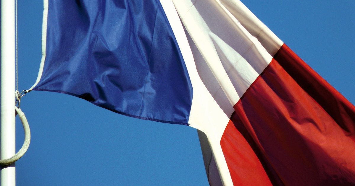 A close-up of the French national flag waving against a clear blue sky in Paris, France.