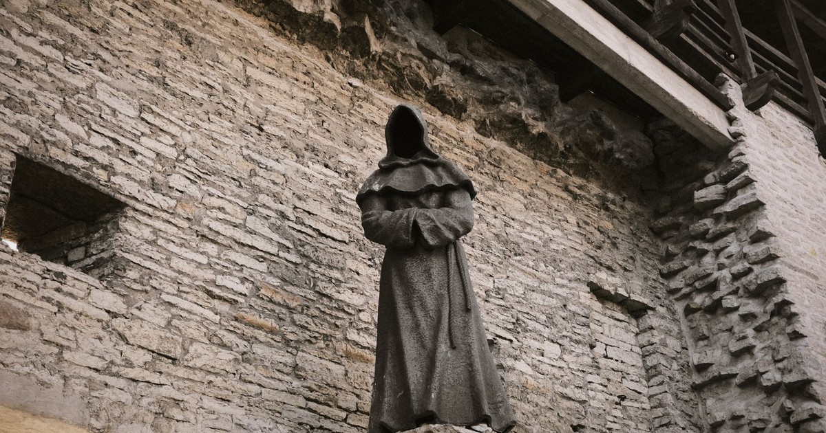 Cloaked statue within an ancient stone wall, exuding a mysterious and historical ambiance.