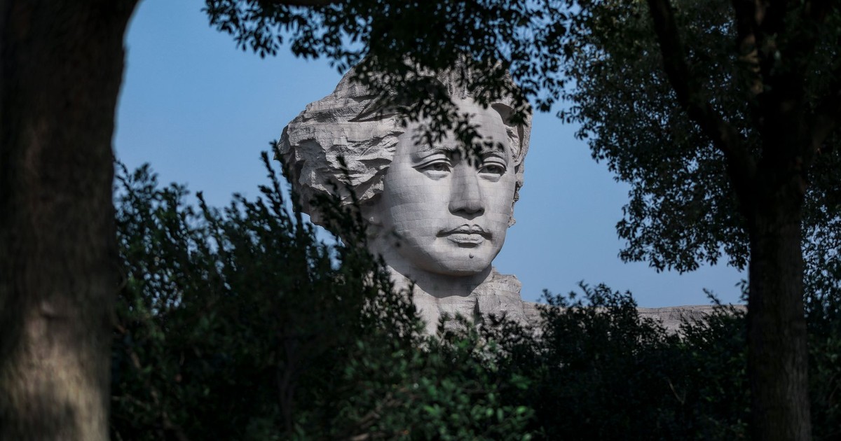 A statue of Mao Zedong emerges through lush greenery, captured in a tranquil outdoor setting.
