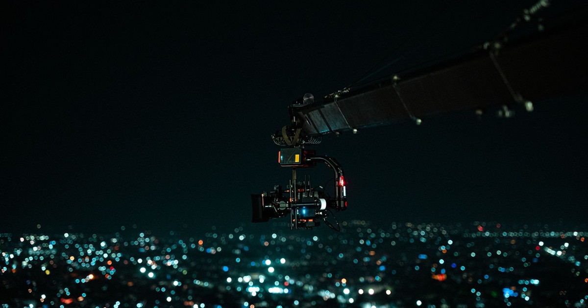 A cinematic drone camera captures a vibrant Indian cityscape at night.