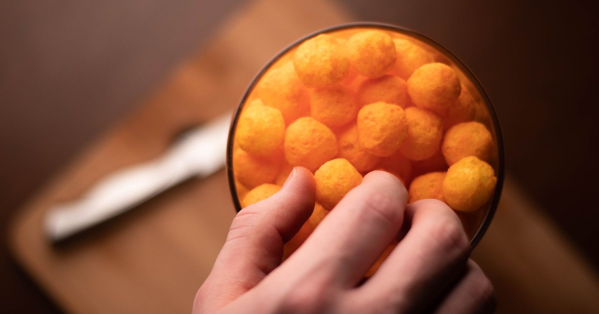 A hand reaching into a bowl of cheese puffs on a cutting board. High angle view.