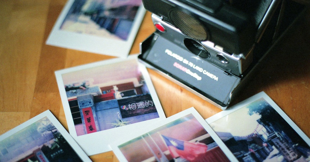 A retro instant camera surrounded by colorful Polaroid photos on a wooden table.