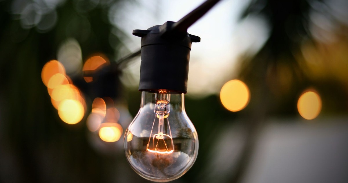 Illuminated light bulb hanging on string with bokeh backdrop outdoors.