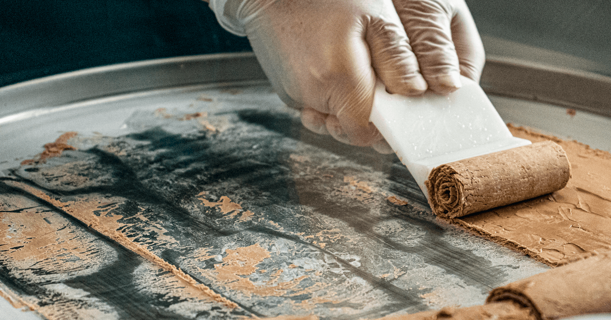 Hands preparing rolled ice cream on a cold metal surface, highlighting food preparation process.