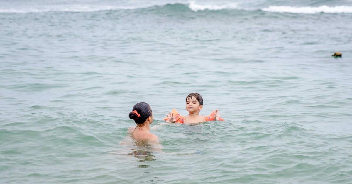 A mother and her child swim in the ocean, enjoying a relaxing day at the beach.