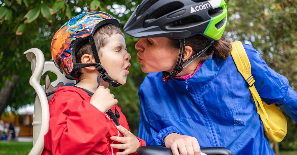 A mother and son share a kiss while wearing safety helmets on a bike ride outdoors.