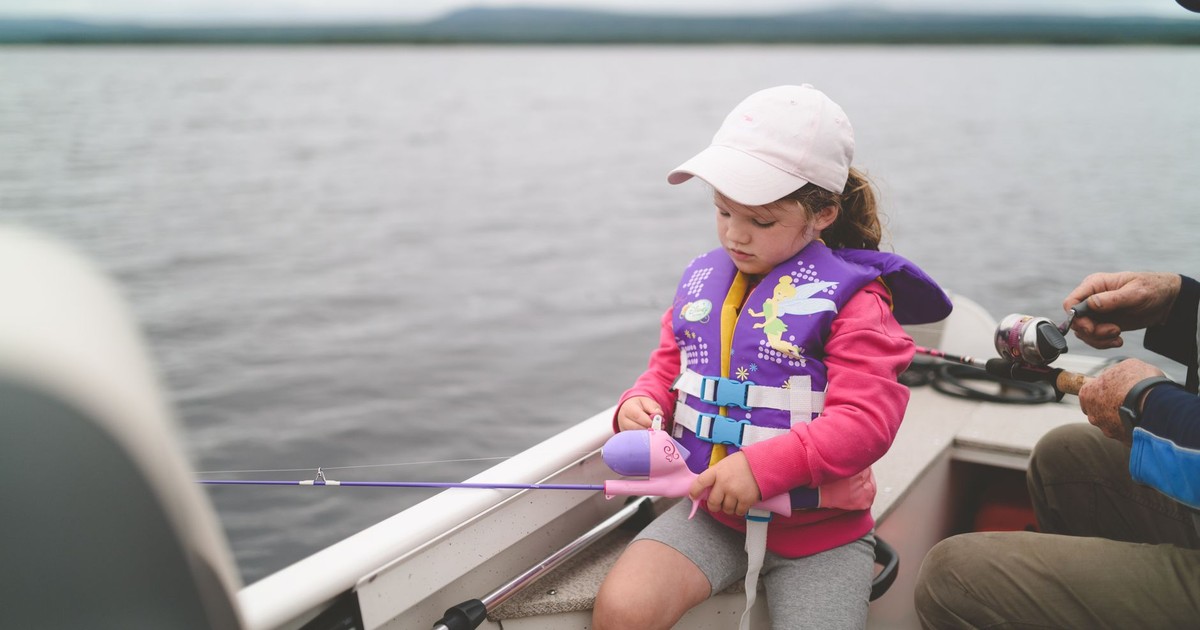A young girl in a life jacket fishing on a tranquil lake, enjoying leisure time.