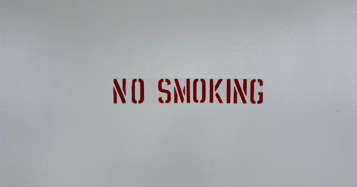 Simple 'No Smoking' sign stenciled on a blank grey wall, promoting a smoke-free environment.
