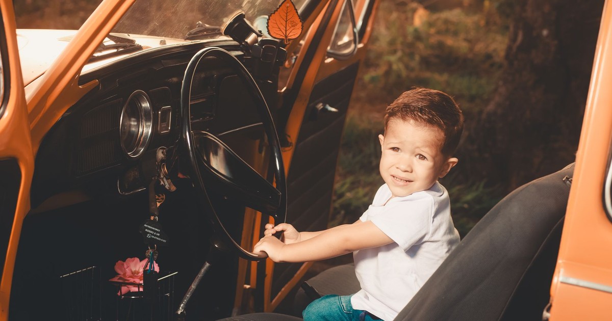 Cute child sitting in an orange vintage car, pretending to drive while looking at the camera.