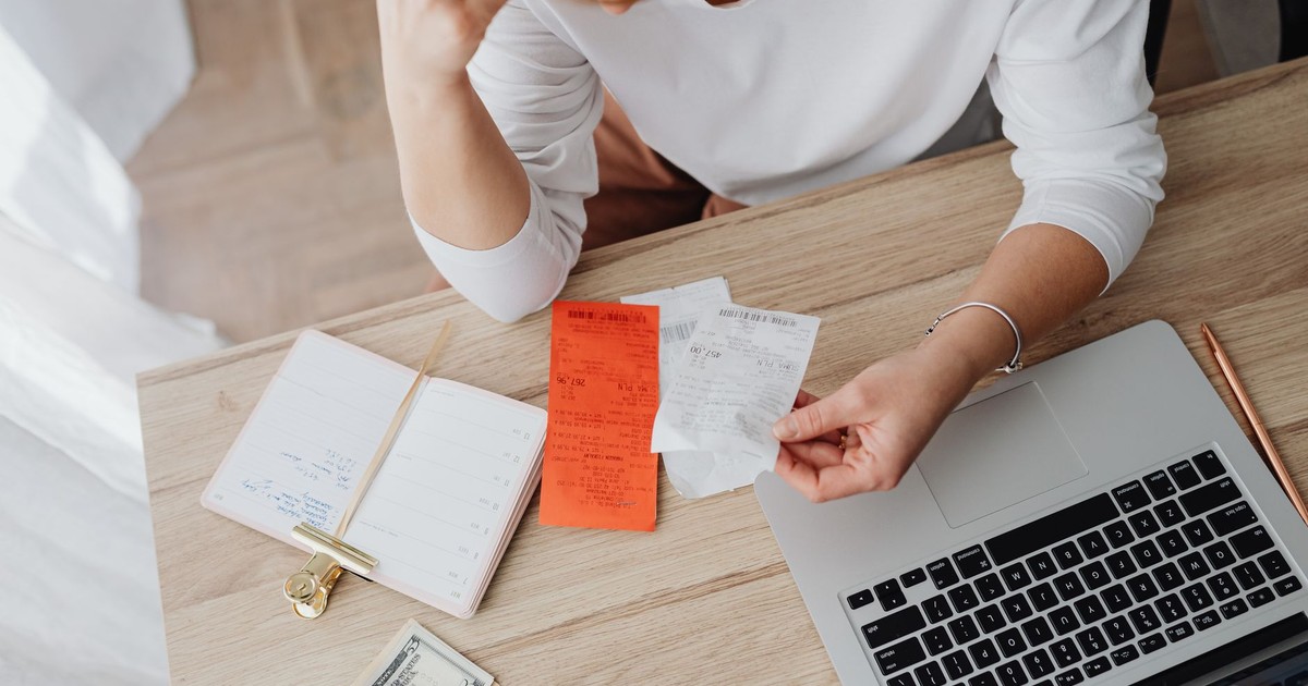 Woman reviewing receipts and planning budget using a laptop and notebook at home to manage expenses.