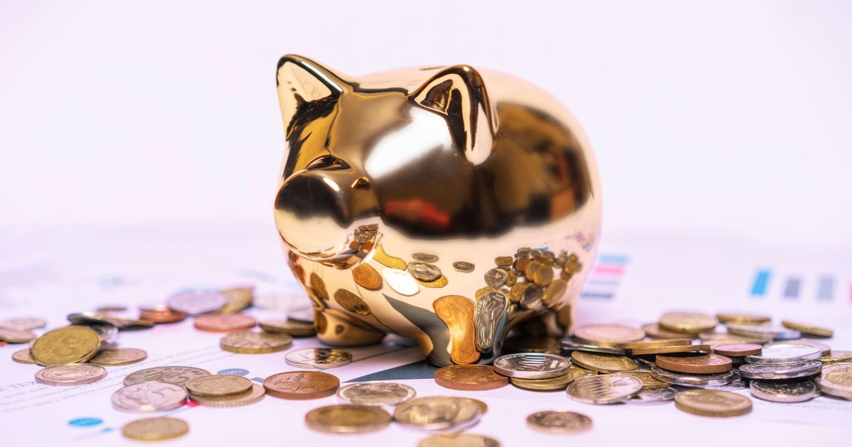 Shiny golden piggy bank on financial documents with scattered coins symbolizes savings.