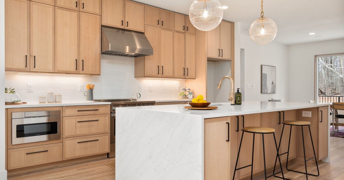 Bright modern kitchen with wood cabinets, marble island, and pendant lights, epitomizing Scandinavian design.
