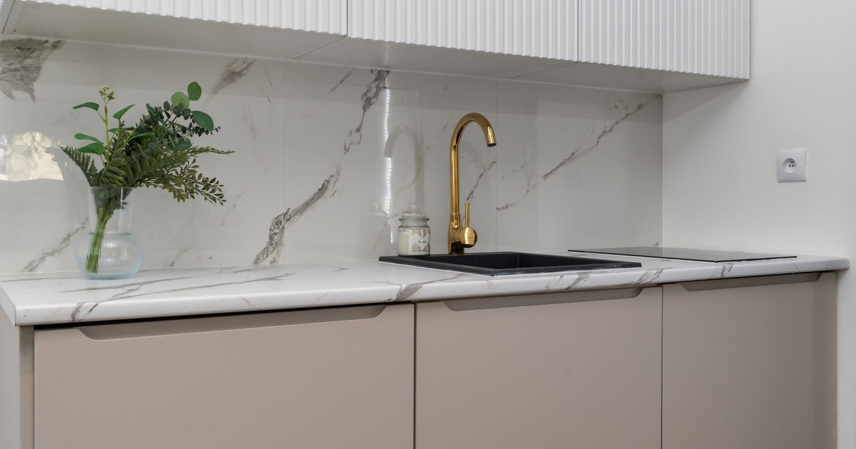 Elegant kitchen interior with marble counters and a gold faucet, featuring greenery for a touch of nature.