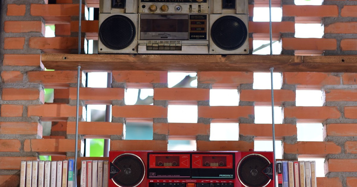 Two vintage radios and audio cassettes displayed on rustic wooden shelves against a brick wall.