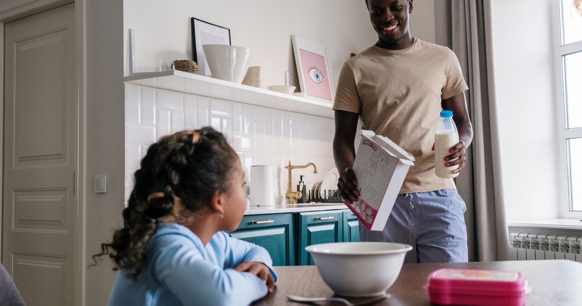 A father and daughter preparing breakfast in a modern kitchen setting, sharing a joyful moment.
