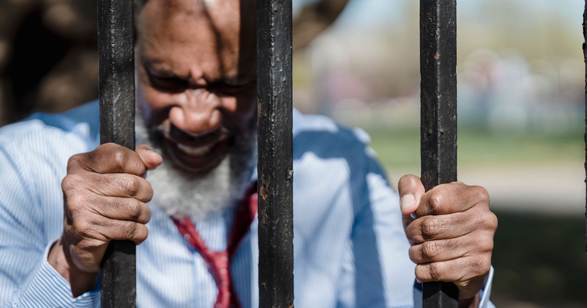 A frustrated man gripping metal bars outdoors, expressing anger and determination.