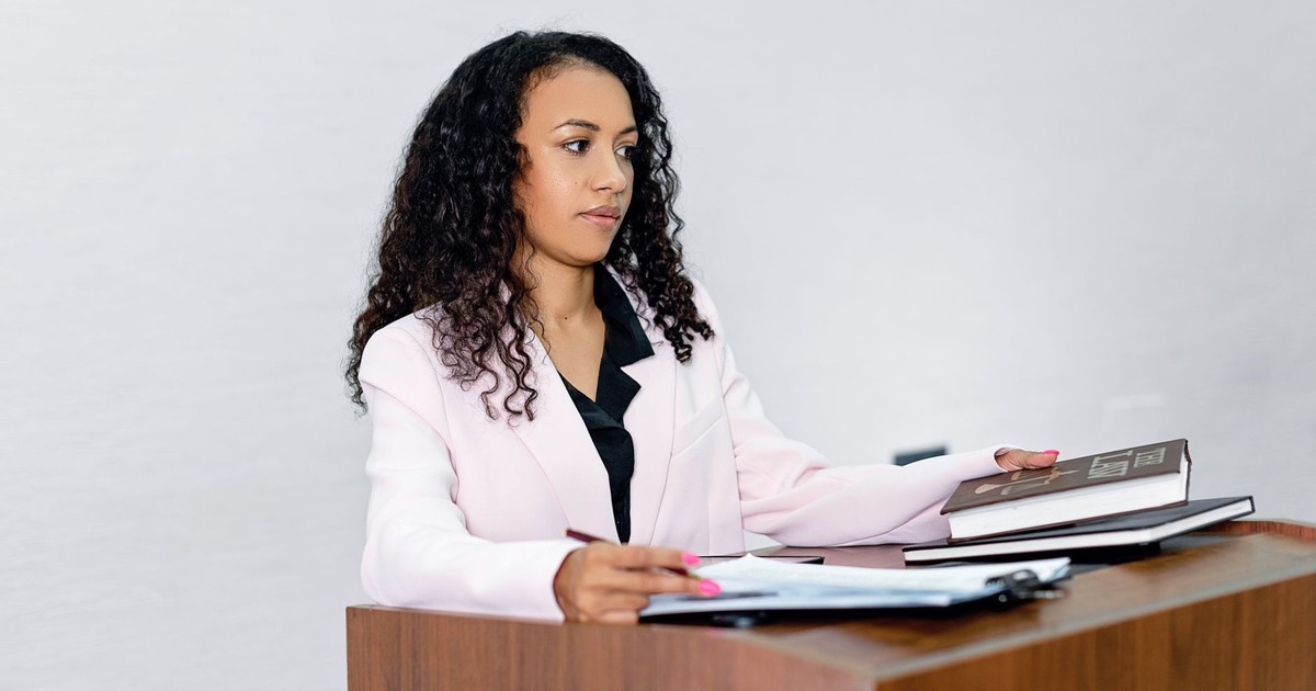 A professional black woman lawyer presenting documents at a podium with books.