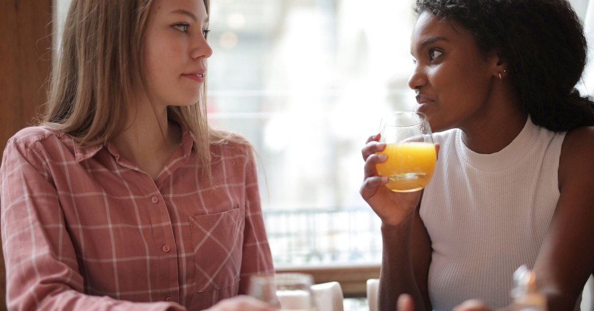 Two women enjoying a casual conversation while drinking orange juice in a café.