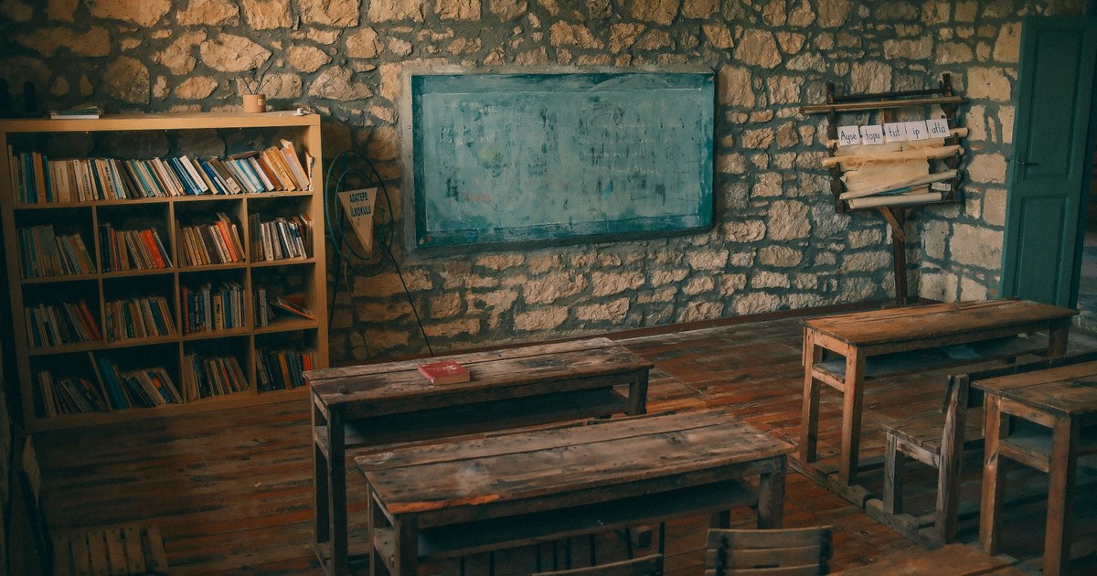 An empty rustic classroom featuring stone walls, wooden desks, and a chalkboard, evoking a sense of nostalgia.