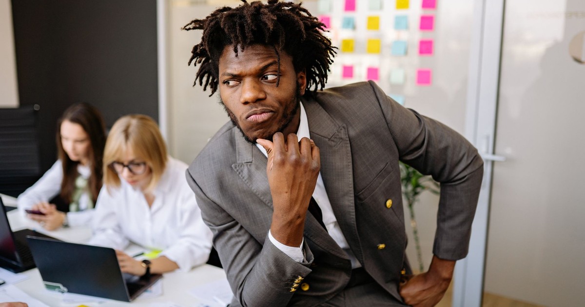 A thoughtful businessman in a suit deep in thought in a bustling office environment.