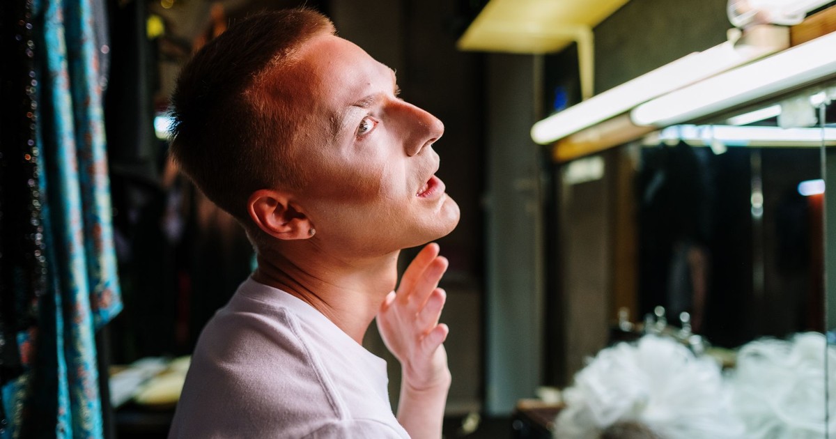 A drag artist capturing a moment of transformation in a theatre dressing room, applying makeup.